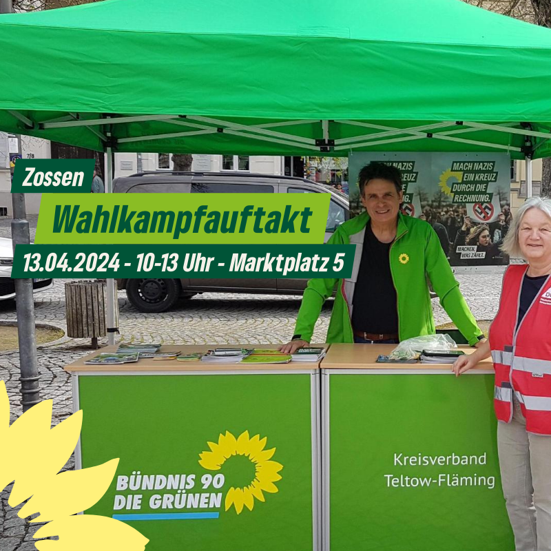 Zwei Personen stehen unter einem grünen Pavillion hinter einer grünen Theke mit der Aufschrift "Bündnis 90 Die Grünen Kreisverband Teltow-Fläming"